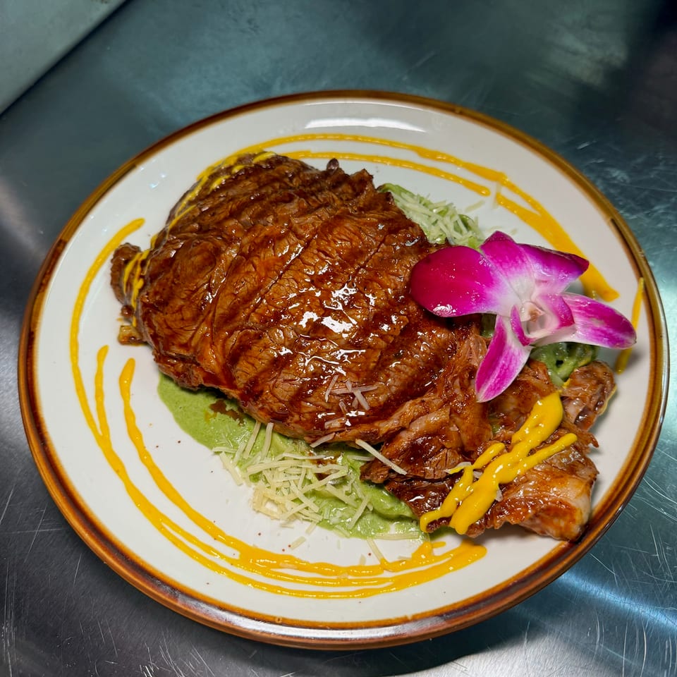 Glazed roasted meat served with green sauce, shredded cheese, pickled radish, vegetables, and yellow sauce on a decorative plate.