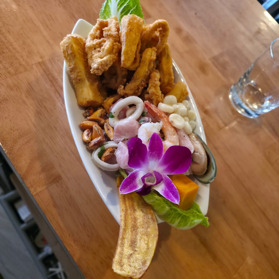 Platter of fried seafood, shrimp, mussels, squid, vegetables, lettuce, and purple orchid garnish on a wooden restaurant table.