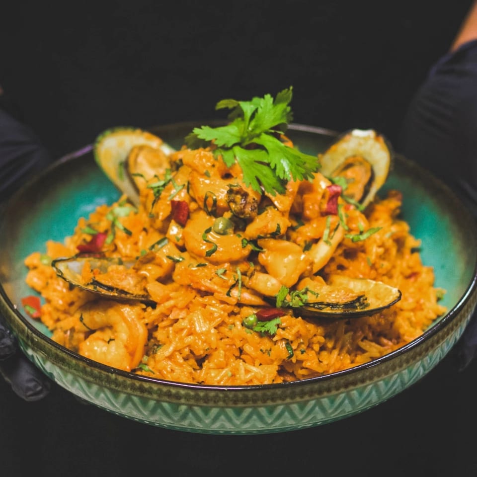 A bowl of orange seafood rice topped with mussels, shrimp, herbs, and red peppers.