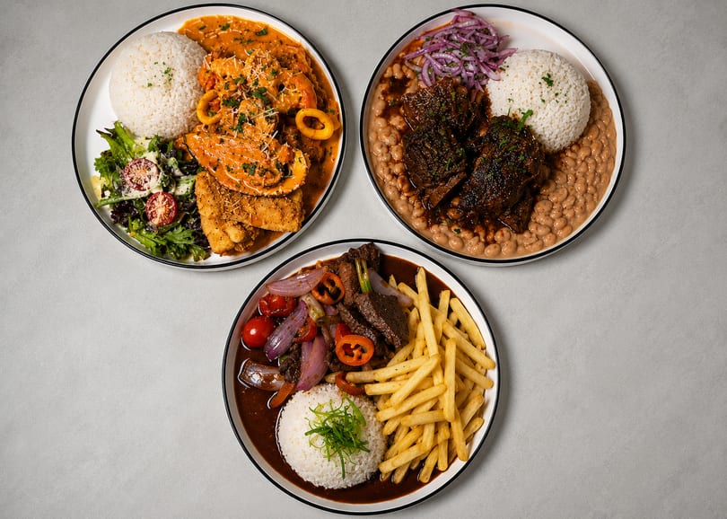 Three plates of Peruvian food, including seafood, beef stew, and lomo saltado, on a white table.