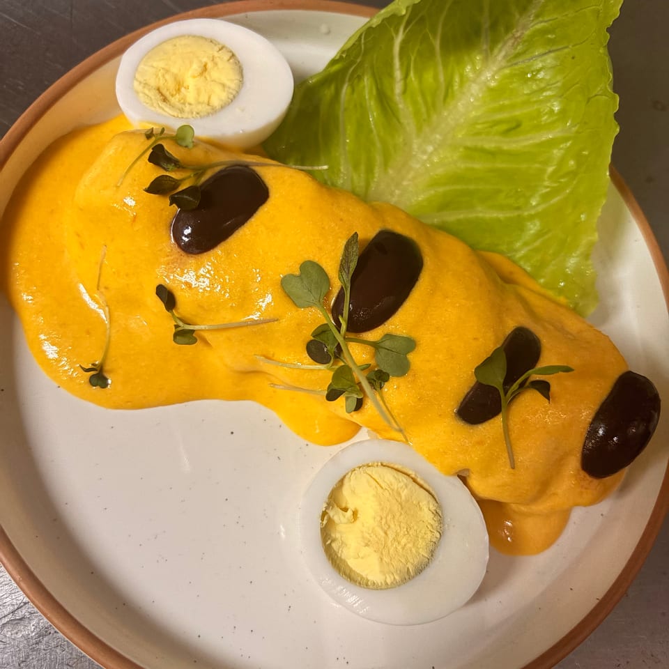Plated orange-sauced dish garnished with black olives, microgreens, lettuce, and halved hard-boiled eggs.