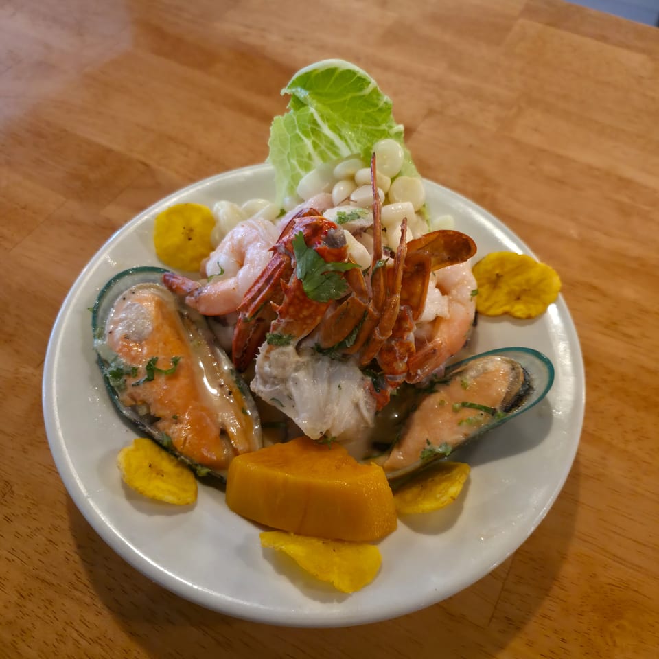Plate of seafood ceviche with shrimp, mussels, corn, plantain chips, lettuce, and cilantro on a wooden table.