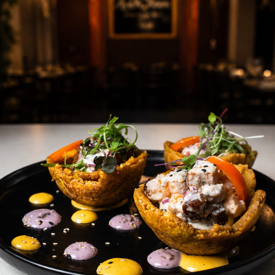 Three crispy edible bowls filled with creamy vegetables and microgreens, arranged on a black plate with colorful sauces in a dimly lit restaurant.
