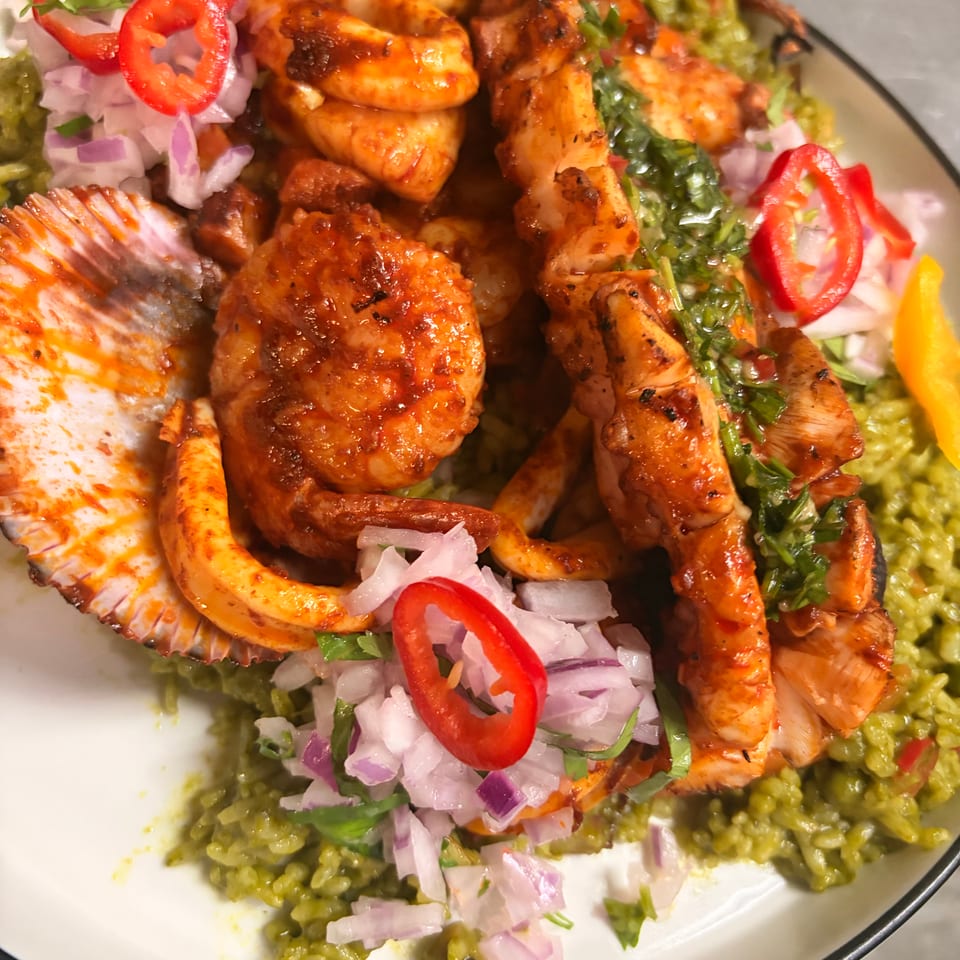 Grilled shrimp, chicken, and vegetables served over green rice with guacamole, chopped onions, cilantro, and red peppers.