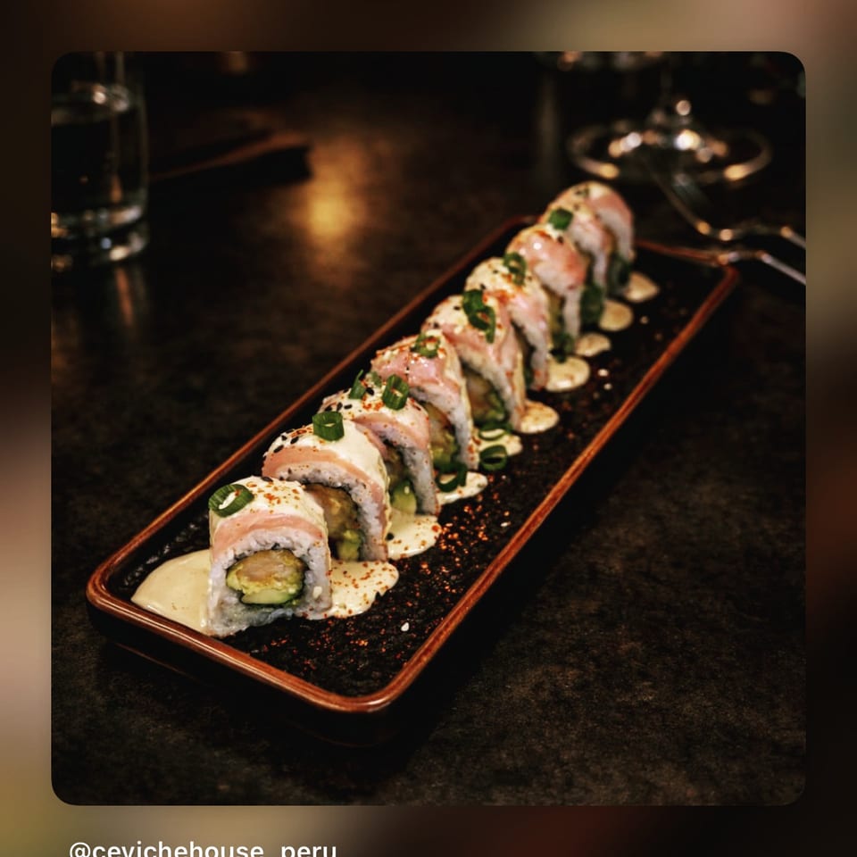 Sushi rolls topped with herbs and creamy sauce arranged on a rectangular platter at Ceviche House Peru.