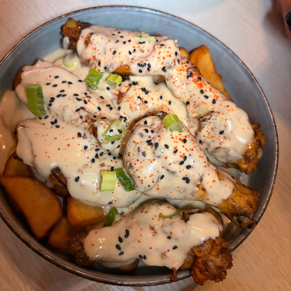Crispy fried chicken and potatoes covered in creamy sauce, black sesame seeds, chili flakes, and sliced scallions on a plate.