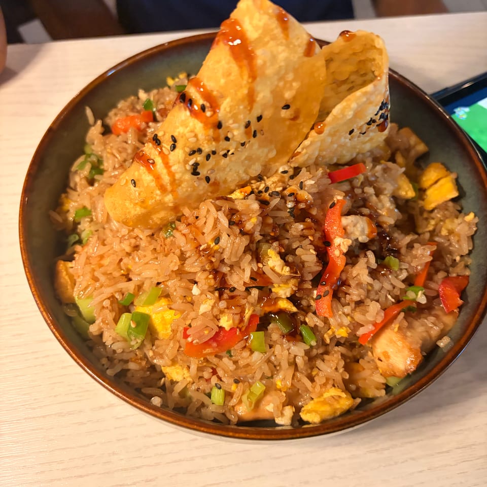 Bowl of fried rice with vegetables, egg, sesame seeds, sauce, and crispy golden wonton triangles.