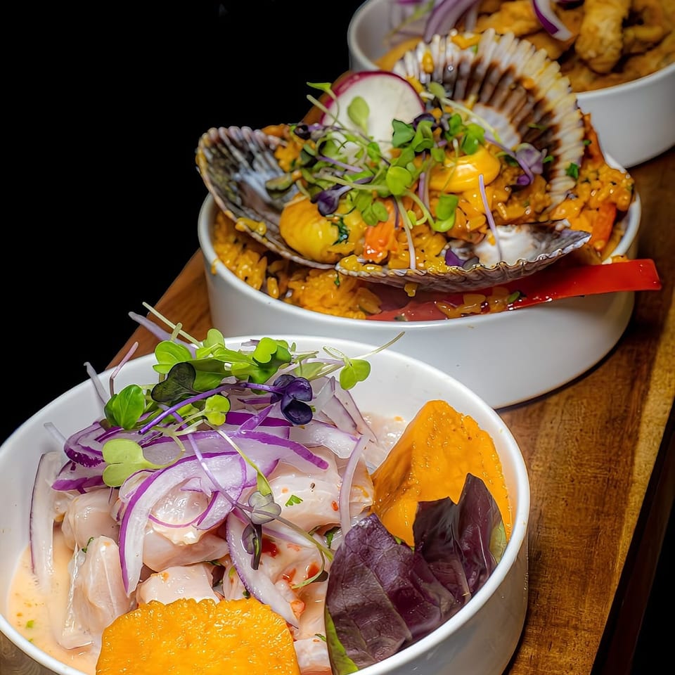 Three bowls of colorful seafood dishes topped with microgreens, red onion, sauces, and sliced vegetables on a wooden table.