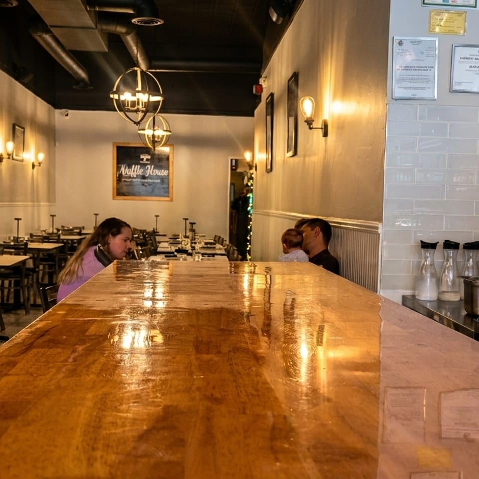 A restaurant interior with a long wooden bar in the foreground and dining tables in the background.