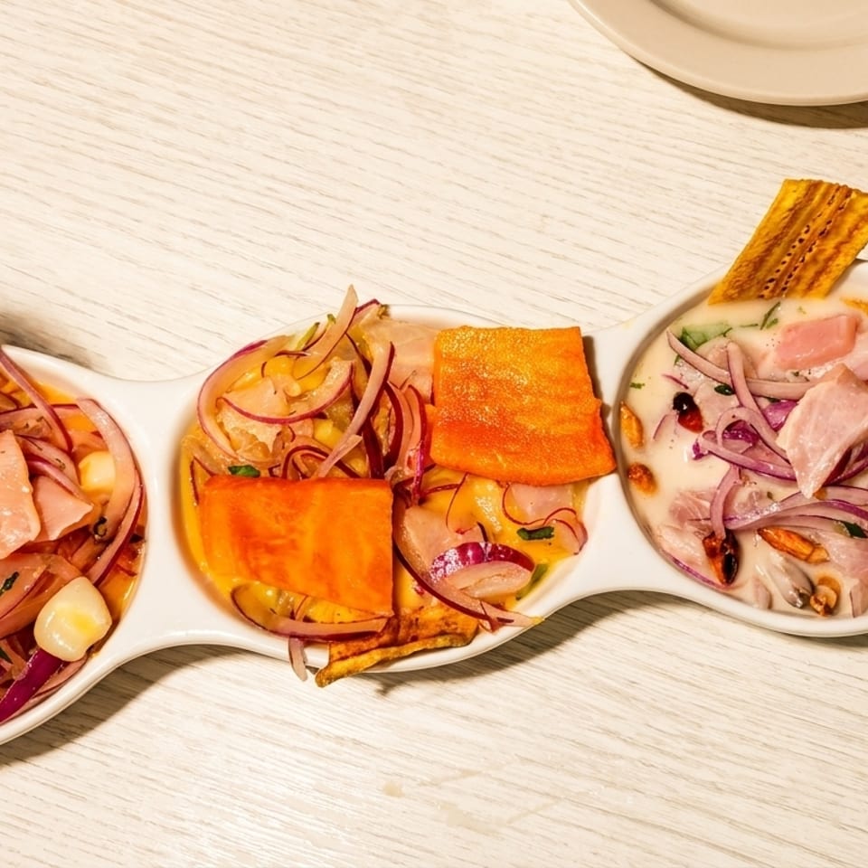 Three servings of ceviche with fish, red onions, corn, and sweet potato in a white dish.