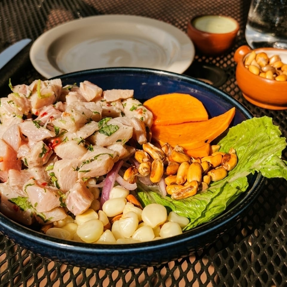 Peruvian ceviche with fish, sweet potato, corn, and lettuce on a dark outdoor table.